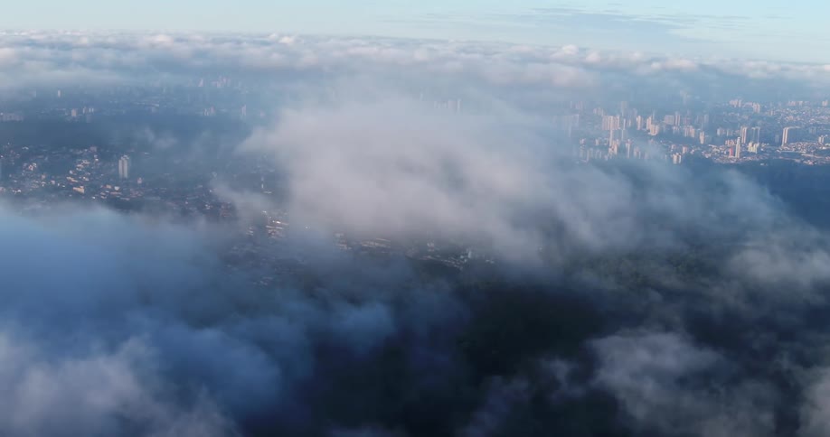 A city and its waterfront become visible from above through a layer of clouds