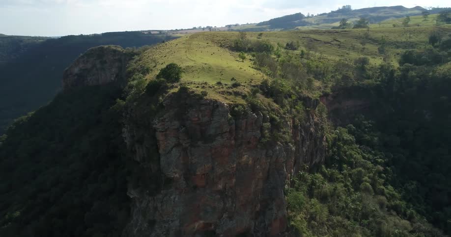 Orbiting aerial view of a cliff on a mountain side covered in green vegetation