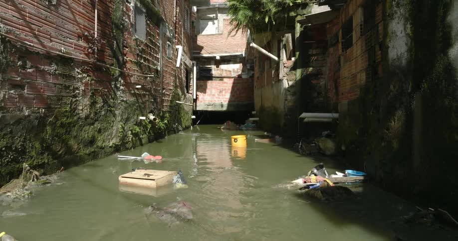 Pvc pipes jutting out from buildings drip into an alley full of water and litter