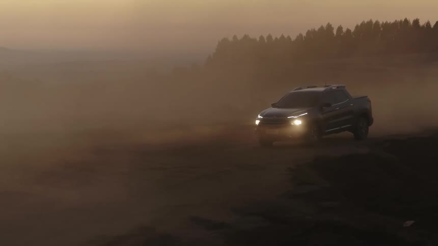 Black pickup truck drives on dusty dirt road in the field at dusk