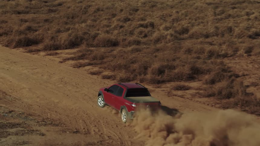 A truck driving off road turns on to a dirt road and causes a large amount of dust to fly up