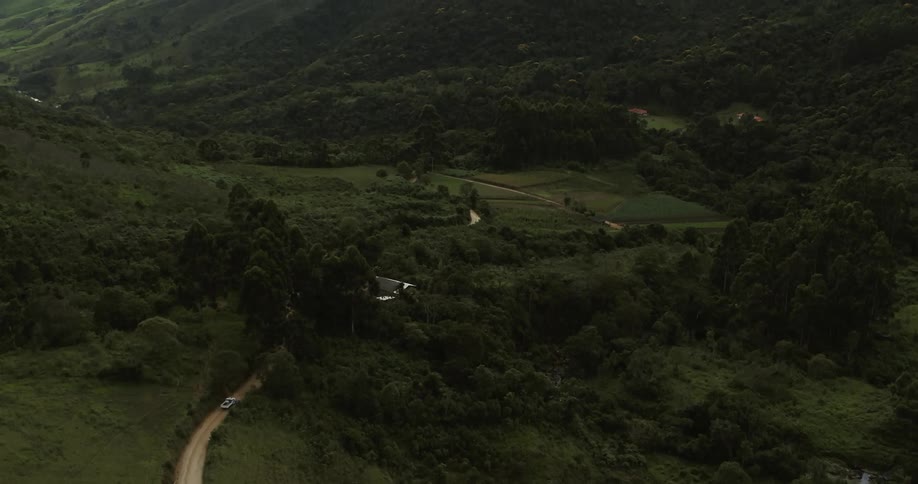 Aerial view of a car driving on road at the slopes of a mountain running through a valley on a rural area