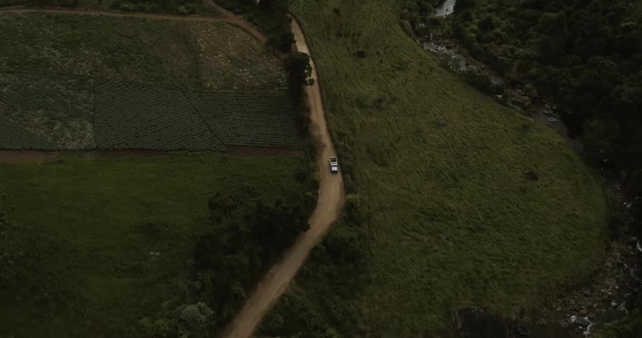 A drone is tracking a truck from high above driving through grasslands with trees grass and a dirt road