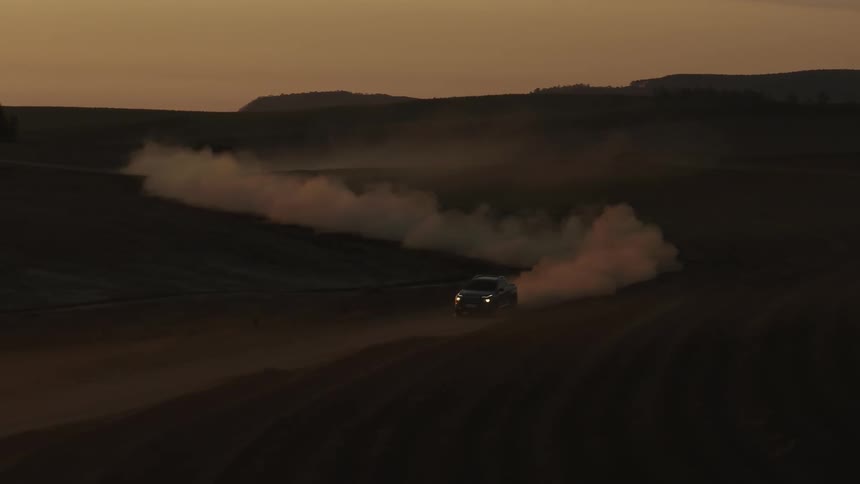 A vehicle leaves a trail of smoke as it drives down a dirt road