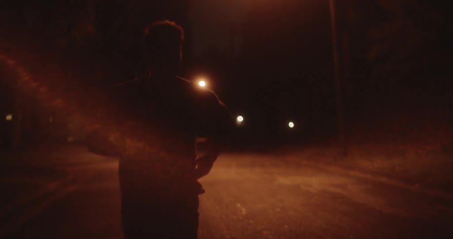 Silhouette of a man jogging on a town street under the streetlights at night