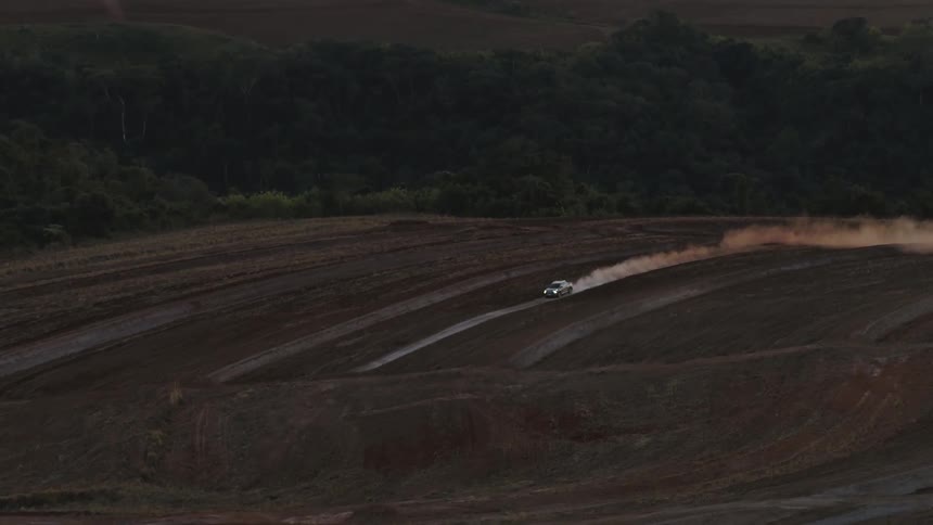 Distant pickup truck drives on dirt road in the field