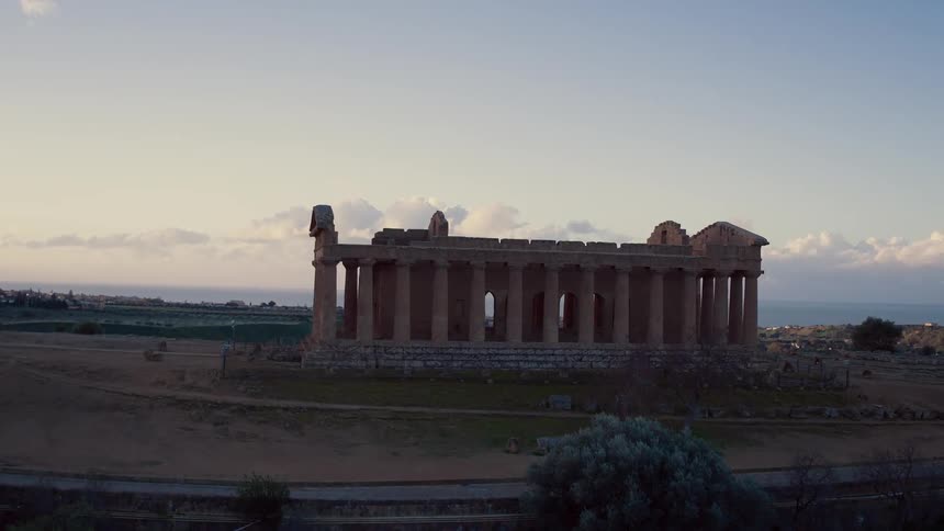 Ruins with stone pillars sit in a rural area at sunset