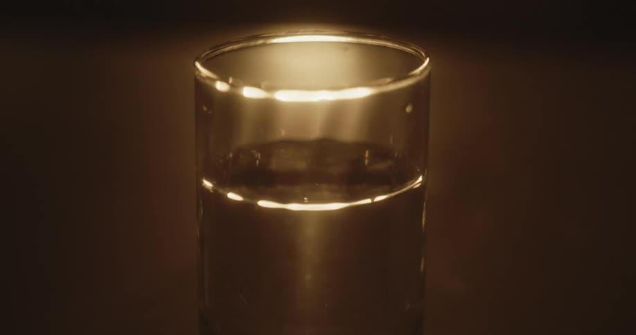 A glass of water is sitting near a light and the water in the glass moves