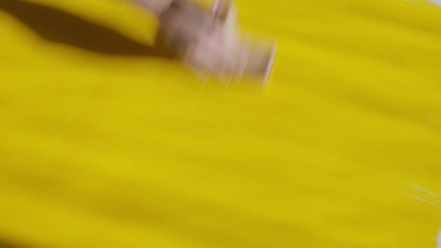 A persons hand is holding a brush and sweeping it up and down across a large yellow painted surface