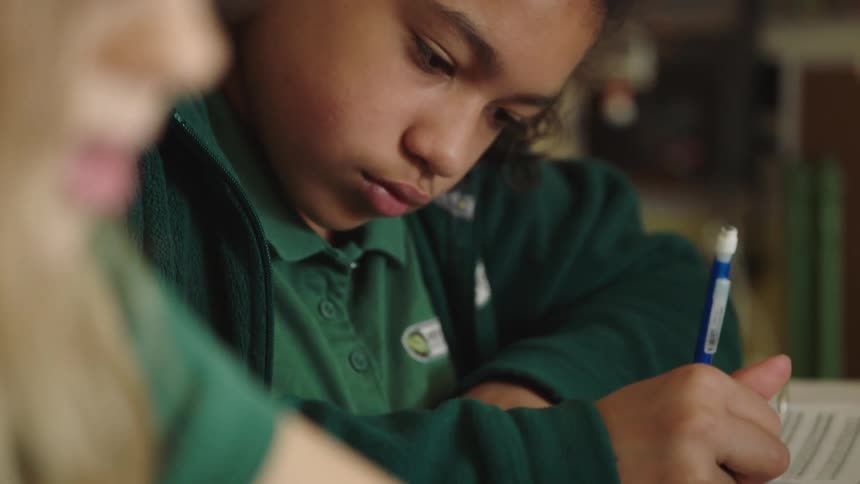 Two students sit at a desk and do school work