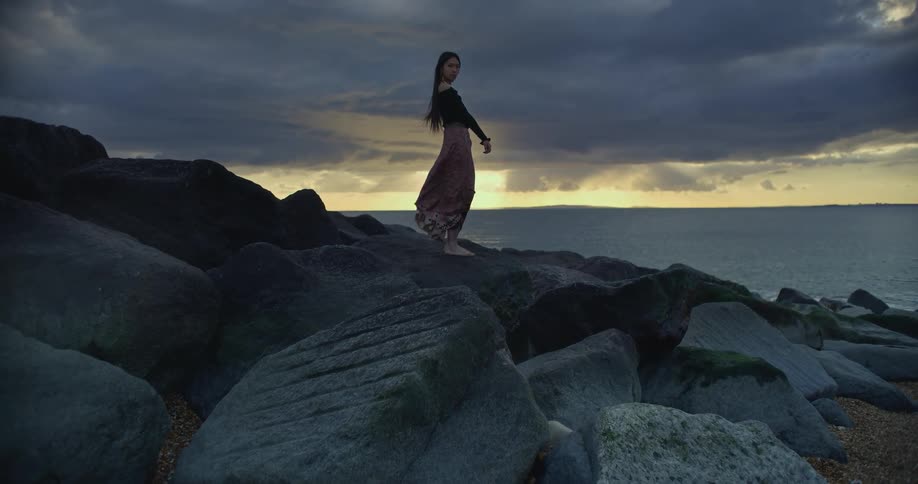 Woman standing on rocks by the sea as the sun sets