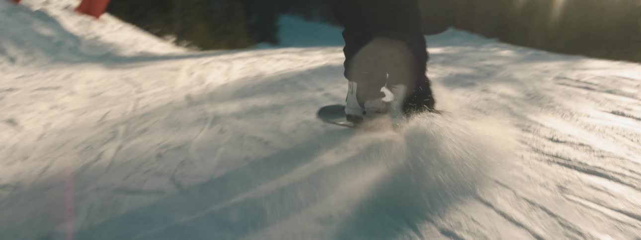 A snowboarder comes to a full stop on a ridge overlooking trees on a sunny day