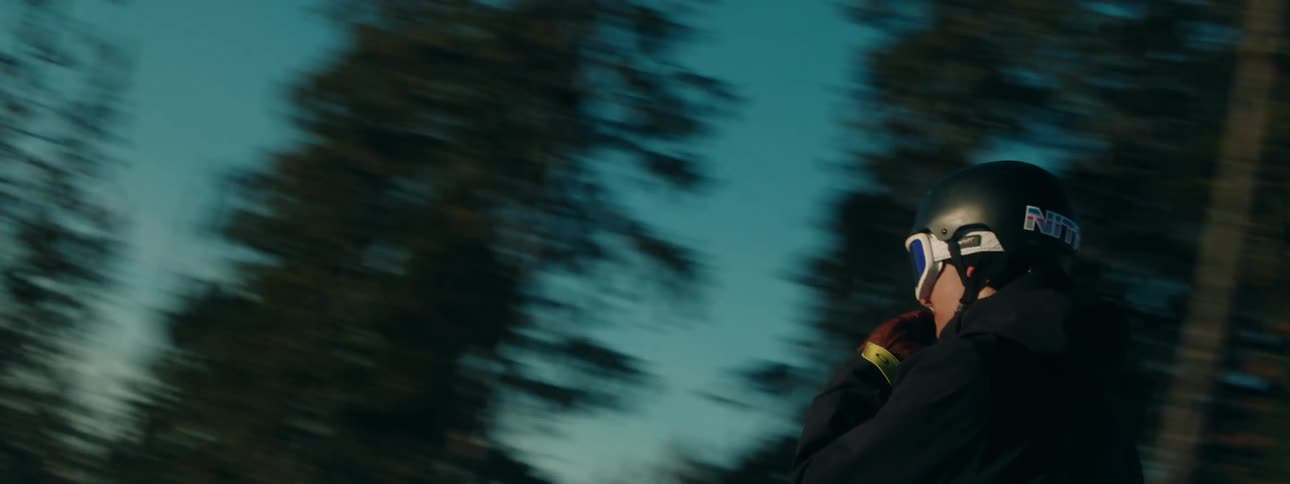 Young woman rides a snowboard on the slopes of a mountain near pine tree forests at evening