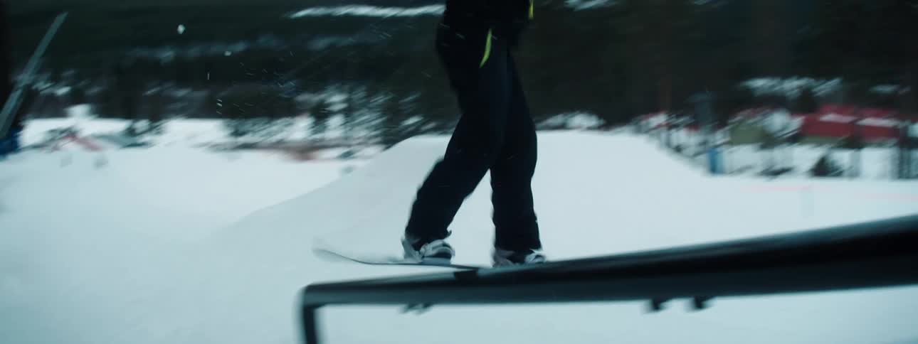 People stand at the top of a ski hill as someone snowboards down and over a railing on the hill
