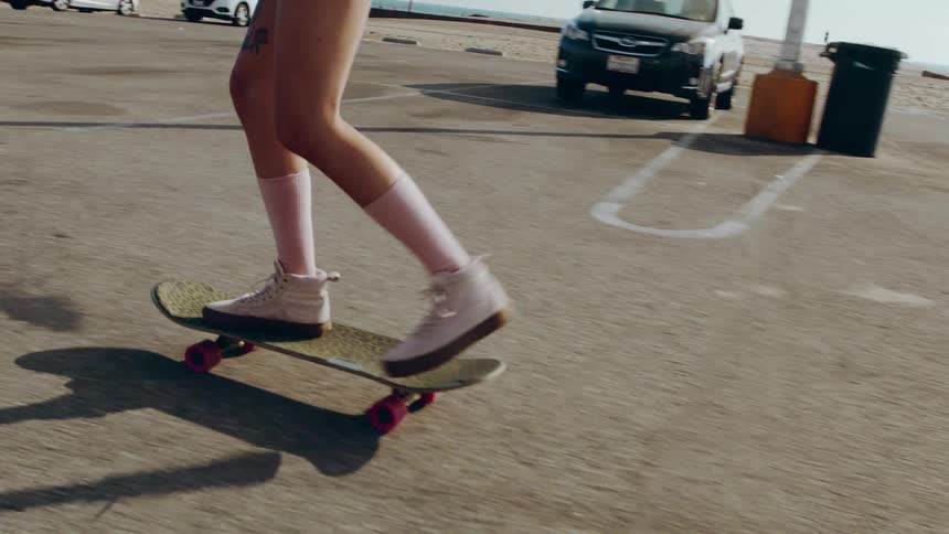Female skateboarder rides skateboard through parking lots near beach