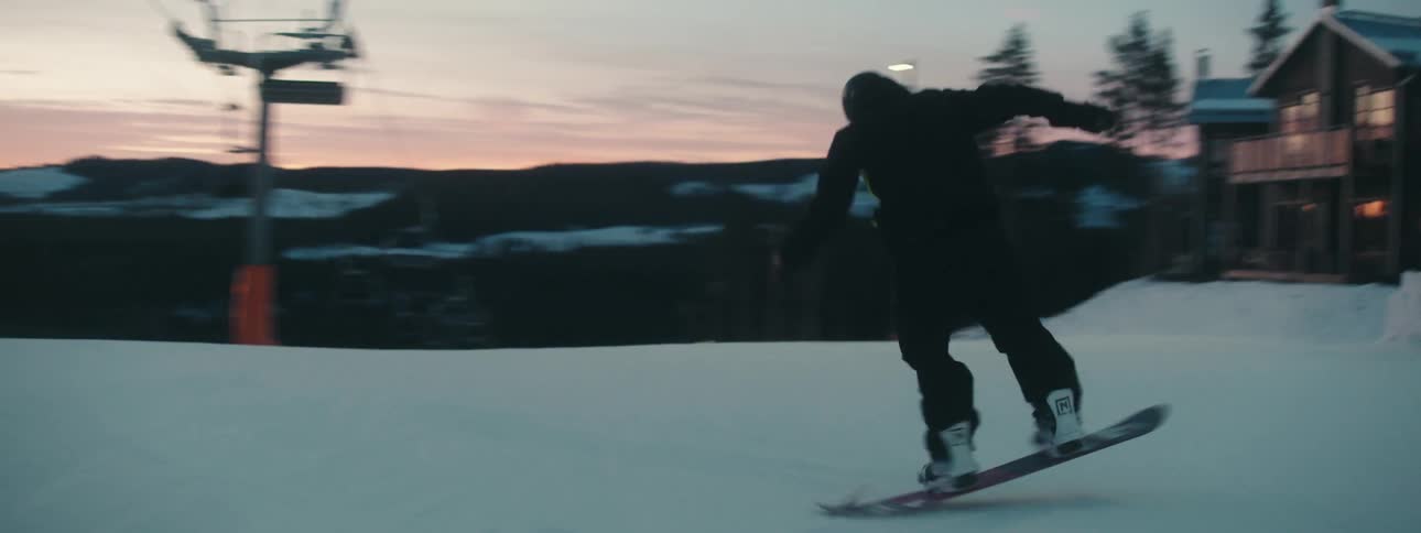 Man wearing helmet goggles snow jacket and pants snowboards at dusk in the resort