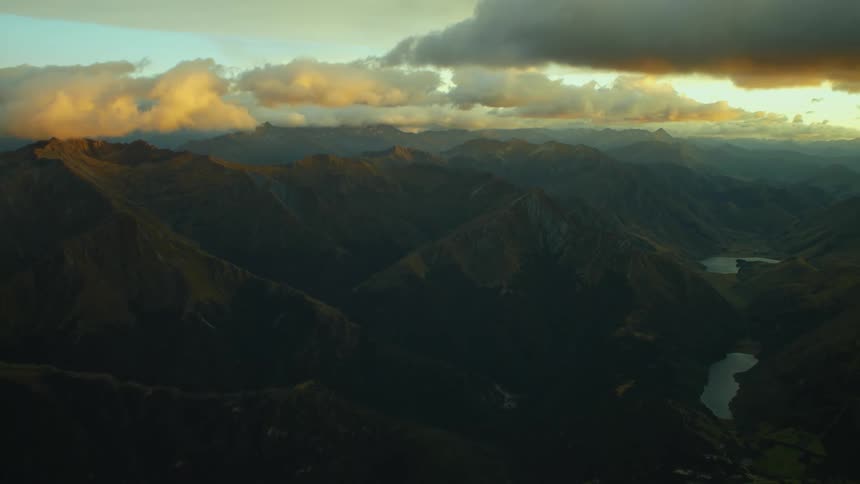 The sun shines on cumulus clouds as they float over mountains with small lakes in the valley