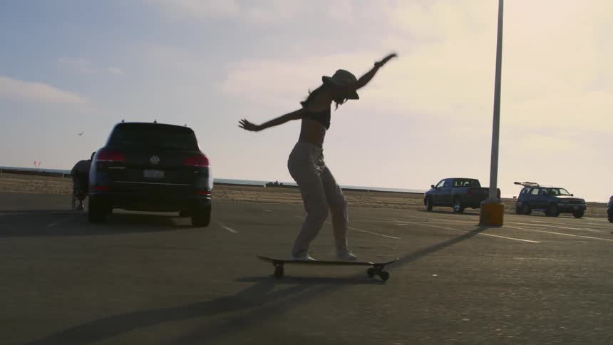 A woman is practicing skateboard tricks in a parking lot