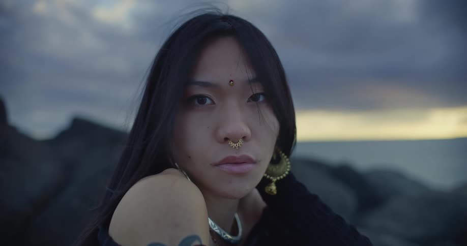 A woman in traditional gold jewellery poses in front of the sea and rocks