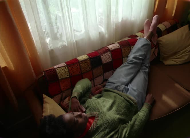 A woman is resting on a couch next to a window