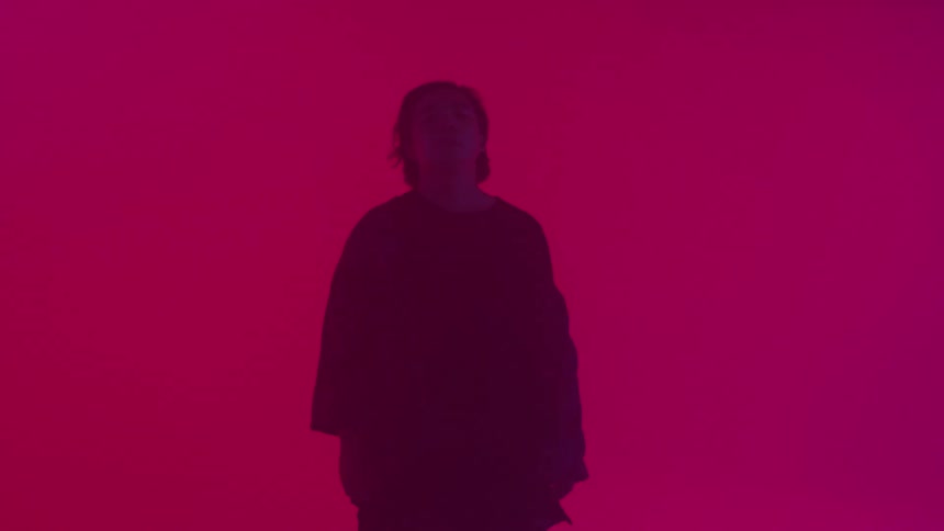 A man stands in a red room with his eyes closed