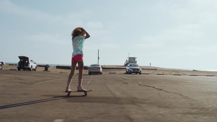 A girl skateboards through a parking lot