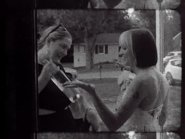 A woman greets her friend with a bouquet of flowers and wine at her front stoop