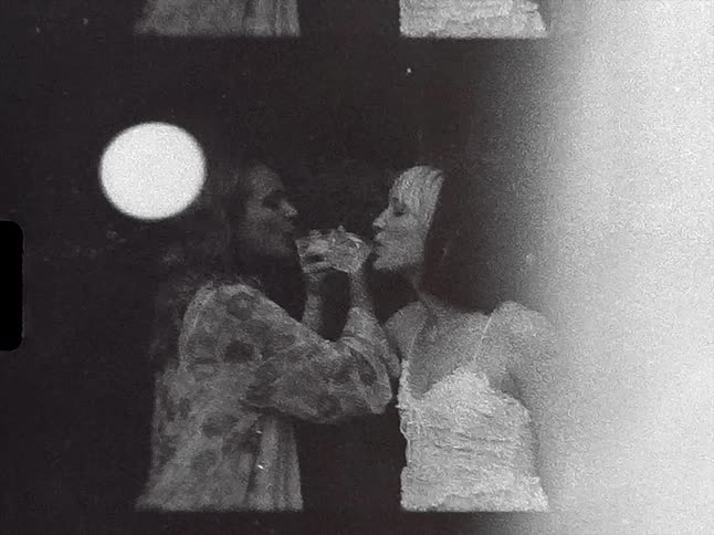 Two female friends toast while drinking with their arms intertwined caught on vintage black and white film