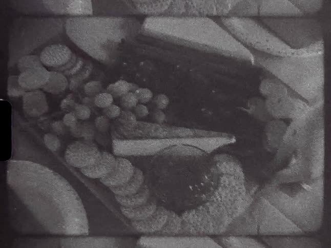 A woman places a platter of food on a dining table before smiling into the camera