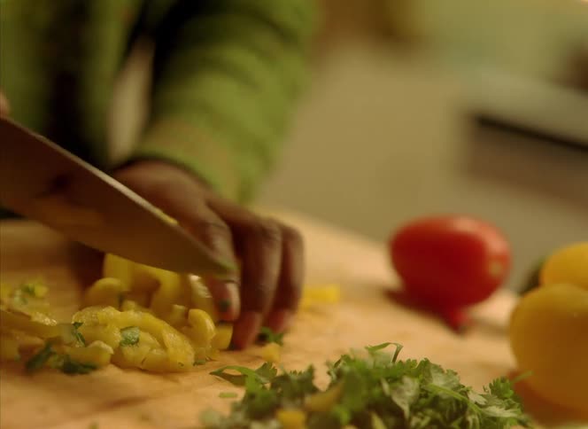 Vegetables are on a cutting board and a woman is cutting them with a knife