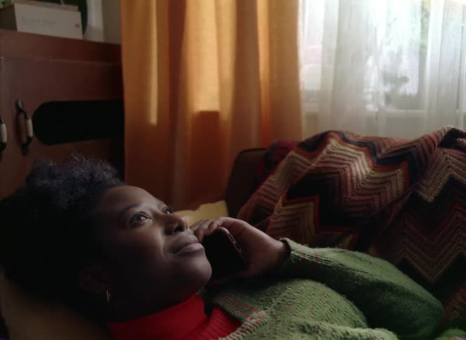 A teenage girl lying down makes a call on her cell phone and smiles as she listens