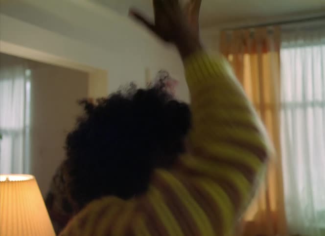 A woman dances into her living room with arms and hands above her smiling face