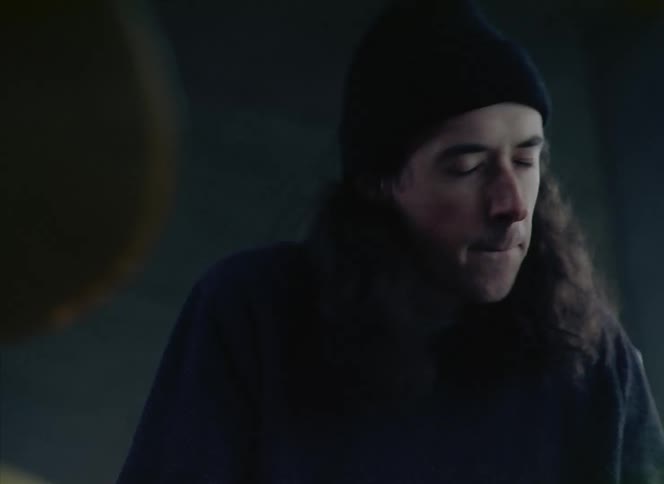 Man with black wooly hat long curly hair and black sweater plays the drum