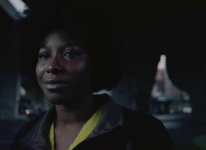 Woman standing outdoors near city street closes her eyes and stretches her neck with a smile
