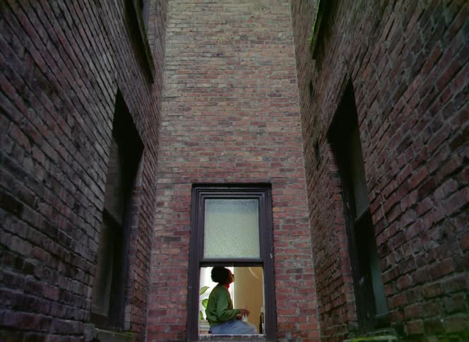 A woman is sitting in her apartment building near a window