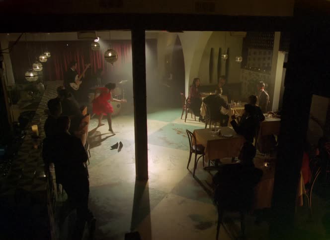 Woman wearing a red dress takes off her high heels shoes and starts dancing on a restaurant