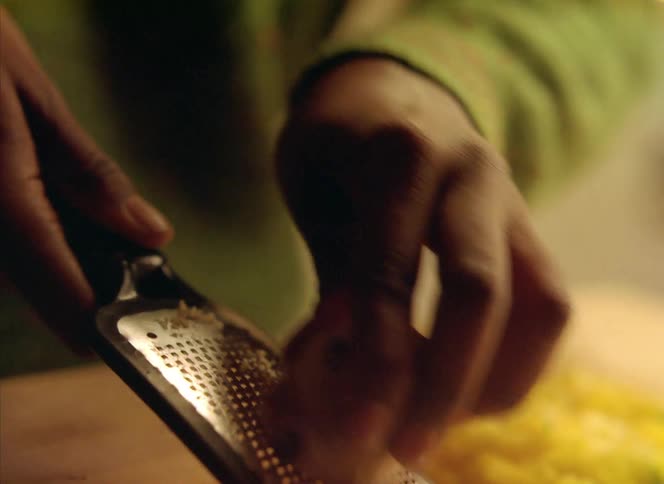 Close up of a person using a small mini grater to grate food in the kitchen at home