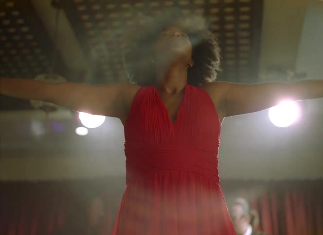 A woman stands in front of a band playing and raises her arms up in the arm as she sways side to side