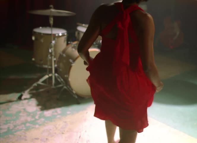 A woman dances under the lights facing a drum set and empty stage