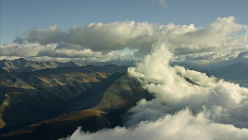 The sun shines on cumulus clouds floating above mountains