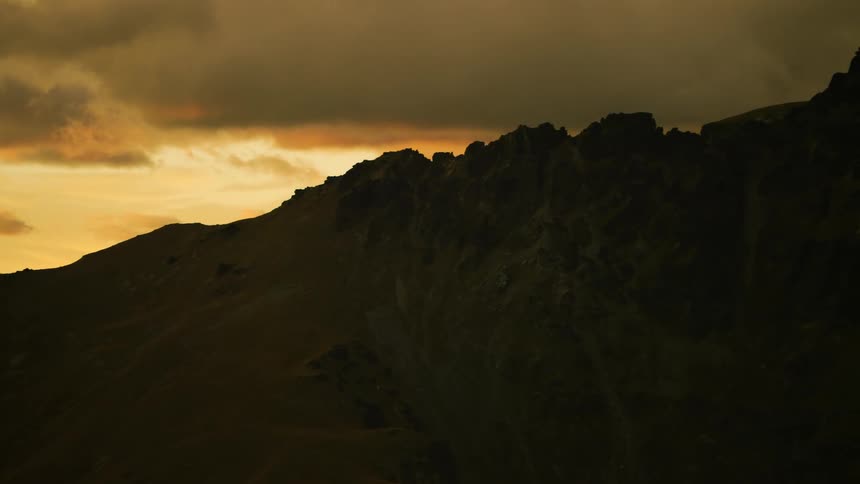 Silhouette of a mountainside in a colorful sky and clouds grow darker near the mountaintop