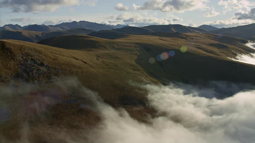 Aerial view of white clouds hovering over the gentle slopes of a mountain range at morning
