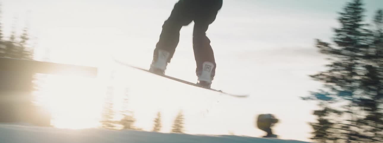 A snowboarder slides up a ramp and across a bar on a snowy mountain slope during the day