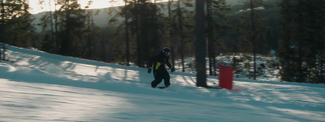 A person rides a snowboard down the snow covered slopes of a mountain at evening