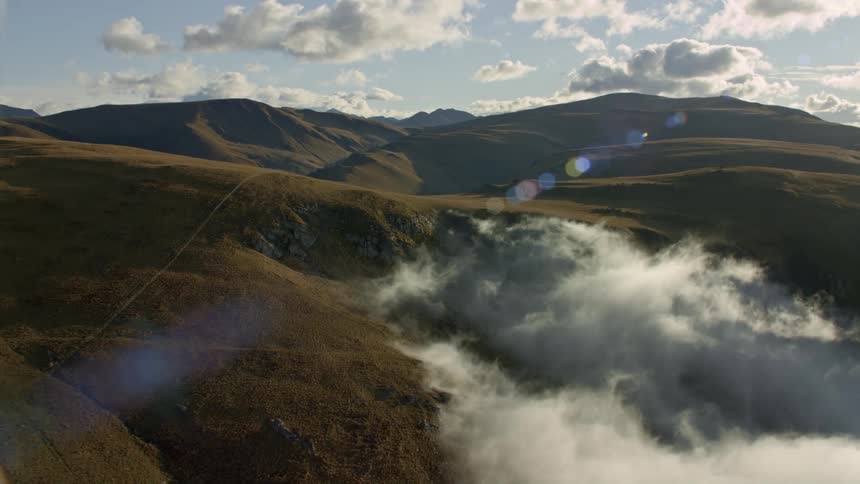 The sun shines upon mountains and hills under a cloudy sky