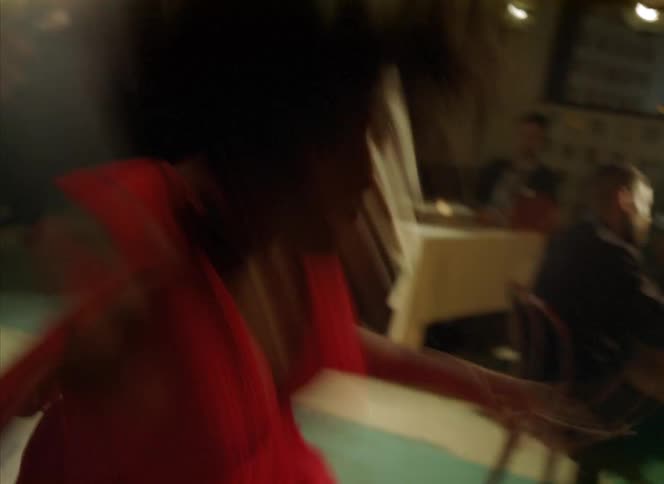 People watch female dancer with curly hair and red dress on stage with drum kit and guitar in front of red curtains