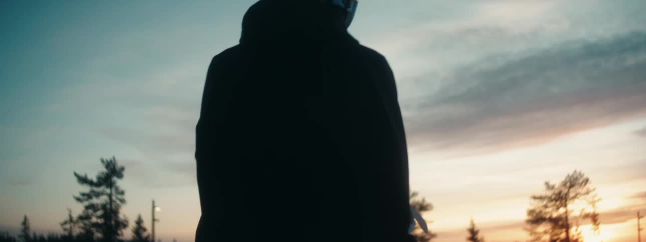 Silhouette of a man dropping a snowboard on the ground near a forest at evening