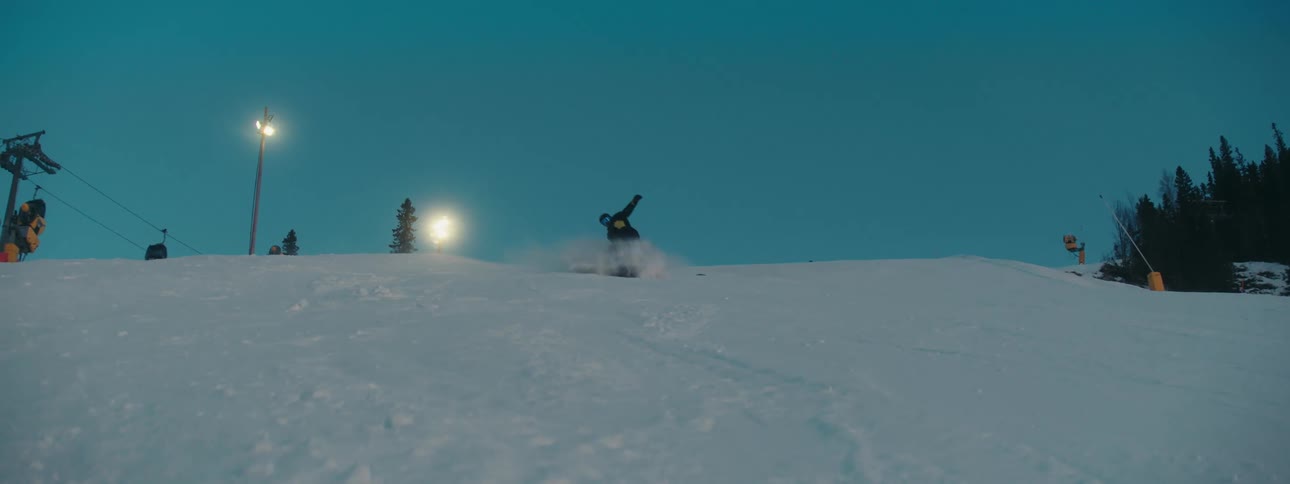 A person descends a ski slope on a snowboard in the evening