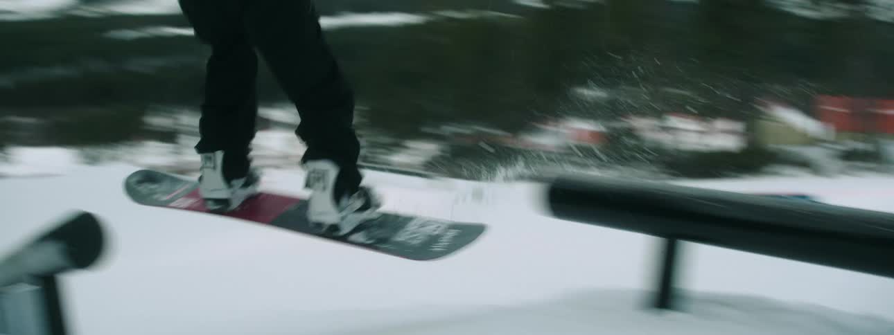 Man riding a snowboard downhill on the slopes of a mountain jumps over rails