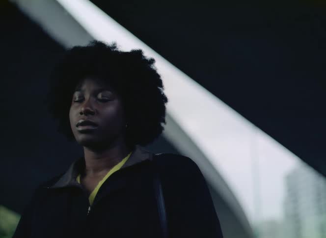 There is a young black women that is standing still in the daytime
